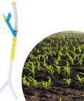 Handy Manual Fertilizer Spreader For Farm Use Time Saving Press Type Tool next to field of corn seedlings.