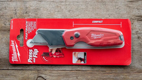 Fastback Compact Folding Utility Knife With Quick Change Blade System in retail packaging on a wooden surface.