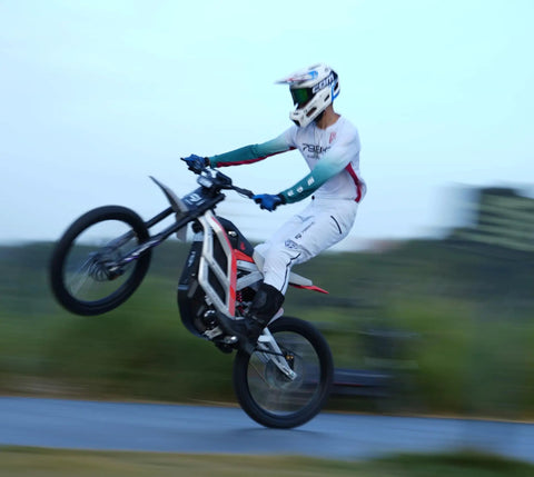 Adult Electric Dirt Bike Built To Shred With Raw Torque And 53 MPH Top Speed performing a wheelie on dirt track.