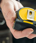 Person holding Fatmax Tape Measure with Blade Armor and Dual Scale 8m Length, Mylar Coated Blade, emphasizing compact design.