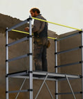 Man using Heavy Duty Aluminum Scaffold Tower Ready To Roll Work Platform Adjustable Utility Scaffolding With Hatch Deck And Guard Rail 500 Pounds Capacity.