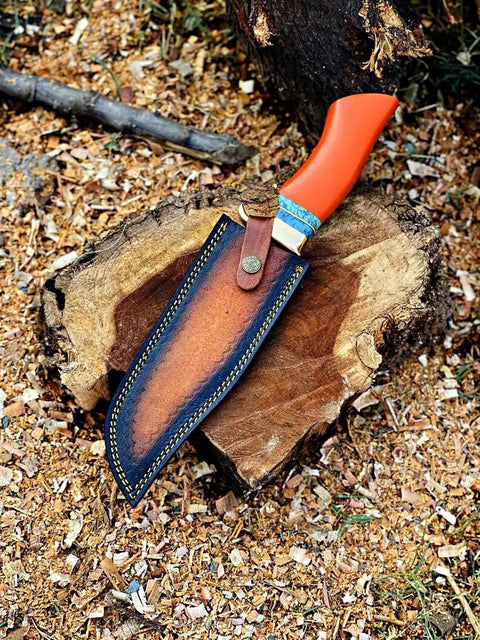Dope Copper Damascus Fixed Blade Knife With Resin Handle And Premium Leather Sheath resting on wooden stump outdoors.