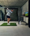 Man using R50 Premium Golf Launch Monitor and Simulator with 10 inch touchscreen, Pro Turf, and Net Return Pro Golf Net setup indoors.