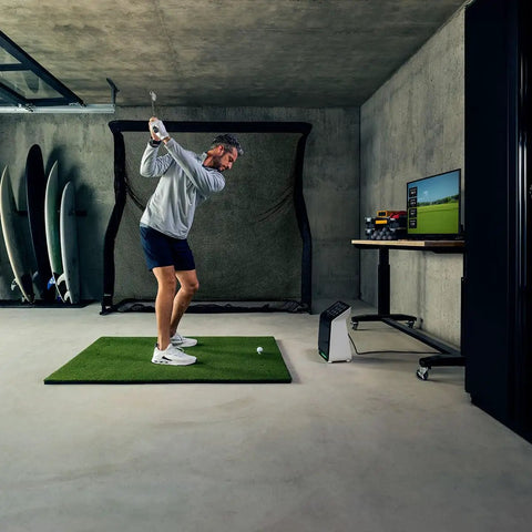 Man using R50 Premium Golf Launch Monitor and Simulator with 10 inch touchscreen, Pro Turf, and Net Return Pro Golf Net setup indoors.