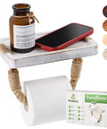 Coastal Rope Toilet Paper Holder With Shelf Wall Mount For Bathroom Decor Rustic Farmhouse White Wood Towel Rack Nautical Style Tissue Roll Holder Ideal For Beachy Coastal Baths, showcasing white shelf with brown bottle and red phone.