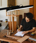 LED Architect Desk Lamp With Clamp illuminating a workspace with a man reading under its 22-inch head, black model for drafting.