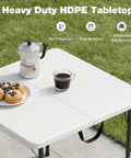 34 Inch Square Folding Table For Four With 330 Lbs Capacity Built Tough HDPE Top And Heavy Duty Steel Legs For Portable Indoor Outdoor Parties Camping White, set with coffee and pastries on a lawn.