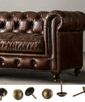 Premium 320 Piece Set Of Top Shelf Upholstery Tacks Featuring A Knockout Antique Brass Finish and Smooth Round Heads displayed with a brown leather sofa.