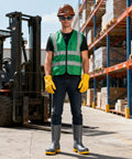 Man in green safety vest, yellow gloves, and grey boots standing in warehouse near forklift. Eye protection for construction.