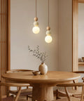 Wabi Sabi Travertine Pendant Light with Wood Ball & Milk Glass Shade hanging over a round wooden table in a cozy dining area.