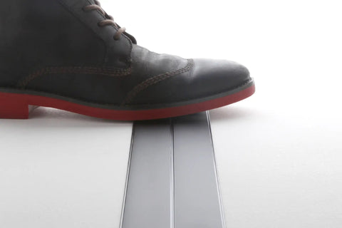 Foot wearing a black boot stepping on Ultra Flat Extension Cord 20 Foot White Power Cable Featuring Paper Thin Build.