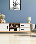 Modern living room with blue wall, white and wood console, black recessed handles, decor items, and artwork on wall.