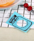 Set of 100 Cute Plastic Candy Bags With Clear Window and Bottle Pattern, blue color on tile surface near cherries and pastry
