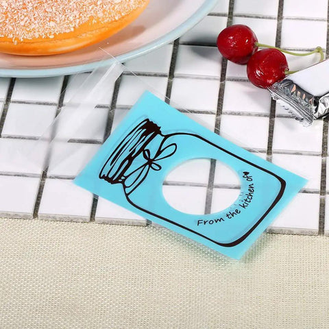 Set of 100 Cute Plastic Candy Bags With Clear Window and Bottle Pattern, blue color on tile surface near cherries and pastry