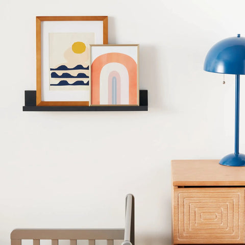 Damage Free Picture Ledge 21 Inch Floating Shelf With Adhesive Strips No Tools Needed Holds Photos And Decorations Up To 5 Pounds Slate Finish includes 1 ledge and 10 strips holding framed art above a wooden cabinet with a blue lamp.