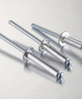 Close-up of Pro Grade Aluminum Blind Rivets Kit With Aluminum Grip And Steel Mandrel Set 80 Piece Fasteners Pack For Home DIY Projects Durable Corrosion Resistant Aluminum Rivets For Indoor And Outdoor Use on metal surface, showing three rivets angled left, highlighting aluminum body and steel mandrel.