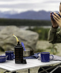 Two Pack 65 Inch Metal Black And Orange Outdoor Torches With Easy Install Lever on a table with blue cups, used in patio setting.