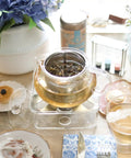 Kyoto 2-In-1 Tea Kettle And Tea Maker Glass Teapot with infuser on table set for tea with flowers and teacups