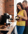 Couple using Pro Game Changer 7 Piece Espresso Essentials featuring 53 Mm Tamper for coffee preparation at home.