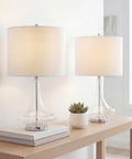 Teardrop Glass Table Lamps Set Of 2 With Clear And Chrome Finish on a wooden table, featuring white linen drum shades