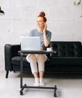 Smooth Rollin Mobile Adjustable Height Portable Computer Desk With Lockable Casters For Top Tier Home Office Standing Laptop Workstation Dark Wood Finish in use with a woman working on a laptop.