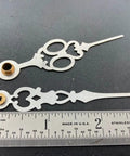 Close-up of brass clock hands replacement kit for 7 inch dial alongside a measuring ruler.