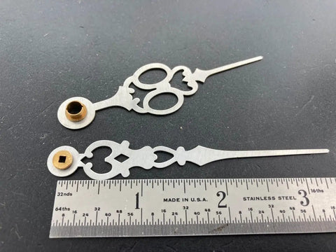 Close-up of brass clock hands replacement kit for 7 inch dial alongside a measuring ruler.