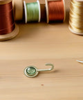 Slick Four Pack Adhesive Wall Hooks For Hanging Towels And Robes With Knockout Grip No Drilling Required Super Quick Mount For Bathroom Kitchen Or Entryway Storage on wooden surface with thread spools.