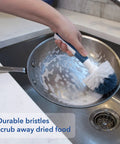 Heavy Duty Sink And Dish Scrub Brush With Safe Bristles cleaning a soapy frying pan in a kitchen sink.