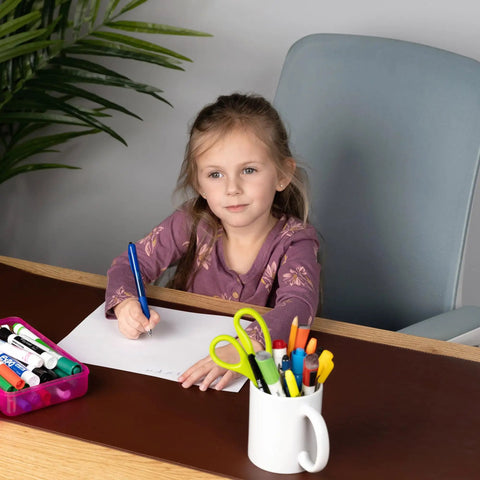 Girl writing on paper with pens on a desk in home office, near XL Desk Pad 17 X 36 Inch Large Vegan Leather Desk Mat For Home Office