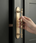 Close-up of hand using Champagne Bronze Cabinet Pulls With Backplates, 2 Pack, 5 Inch Center to Center, on dark cabinet.