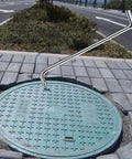 No Sweat Stainless Steel Manhole Hook Tool For Storm Drain Covers And Septic Tank Opener With Ergonomic T Handle positioned above manhole.