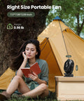 Woman reading by a tent with a Portable Camping Fan With LED Lantern, 360 Degree Rotation, Clip On For Desk Or Tent nearby.