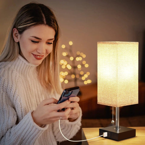 Woman using phone by lit Set Of 2 USB Nightstand Lamps With Grey Fabric Shade Small Table Lamps For Bedroom End Table Living Room Or Home Office Built In 5 Volt 2 Amp USB Ports To Charge Two Devices While You Sleep