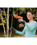 Woman using Premium 18V Cordless Hand Grass Trimmer With 2Ah Lithium Battery for cutting branches in garden.
