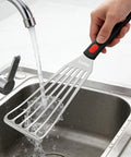 Angled front view of a 10.3-inch stainless steel fish spatula with a slotted head and black handle under running water.