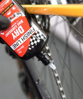 All In One Drivetrain Care Kit With Grunge Brush Dry Lube And EcoTech Degreaser For Cyclists Who Want Quick Clean Smoother Shifts Pro Grade Chain Lubrication And Peak Gear Performance On Every Ride, bottle applying lube to bike chain
