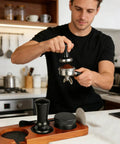 Portable Espresso Tamper Kit For 51Mm Filter Cups, man tamping coffee grounds in kitchen with 7 piece accessory set.