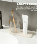 Two Pack Beige Diatomite Soap Dryers Rapid Absorbing Countertop Organizers with toothbrush and toothpaste on bathroom sink.