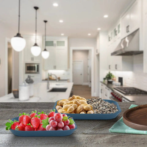 Variety of fruits, peanuts, and sunflower seeds in trays on a wooden table in a modern kitchen setting.