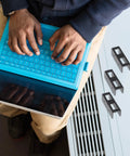 Person typing on a tablet in a blue case, with Super Tight Black Steel Laptop Stand With Storage Tray For Sick Desk Setup nearby.