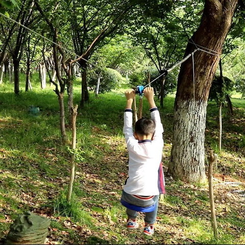 Child playing on Backyard Zip Line Kit 75 Ft For Kids And Adults, Ultra Safe Swing Seat With 60 Mm Thick Cushion, in forest setting