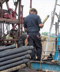 Workers operating drilling equipment at a construction site with heavy machinery and tubular pipes in view.