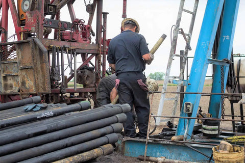 Workers operating drilling equipment at a construction site with heavy machinery and tubular pipes in view.