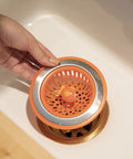 Hand placing Splash Kitchen Sink Strainer Basket Fits All Standard Sinks 4.5 Inch Stainless Steel Orange Fish Drain Cover.