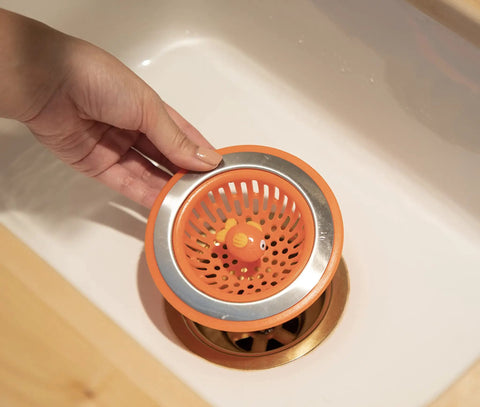Hand placing Splash Kitchen Sink Strainer Basket Fits All Standard Sinks 4.5 Inch Stainless Steel Orange Fish Drain Cover.