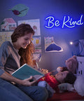 Mother reading bedtime stories with blue 'Be Kind' neon sign glowing in child's bedroom.