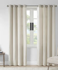 Neutral colored curtains hanging on a window in a cozy living room with a side table and chair.