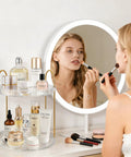 Woman using makeup before mirror with 360 Degree Rotating Makeup Organizer Two Tier No Brainer Large Capacity Tray for skincare and perfume.
