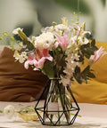 Decorative flowers in geometric black metal cage lampshade vase, displayed on a soft beige cushion background